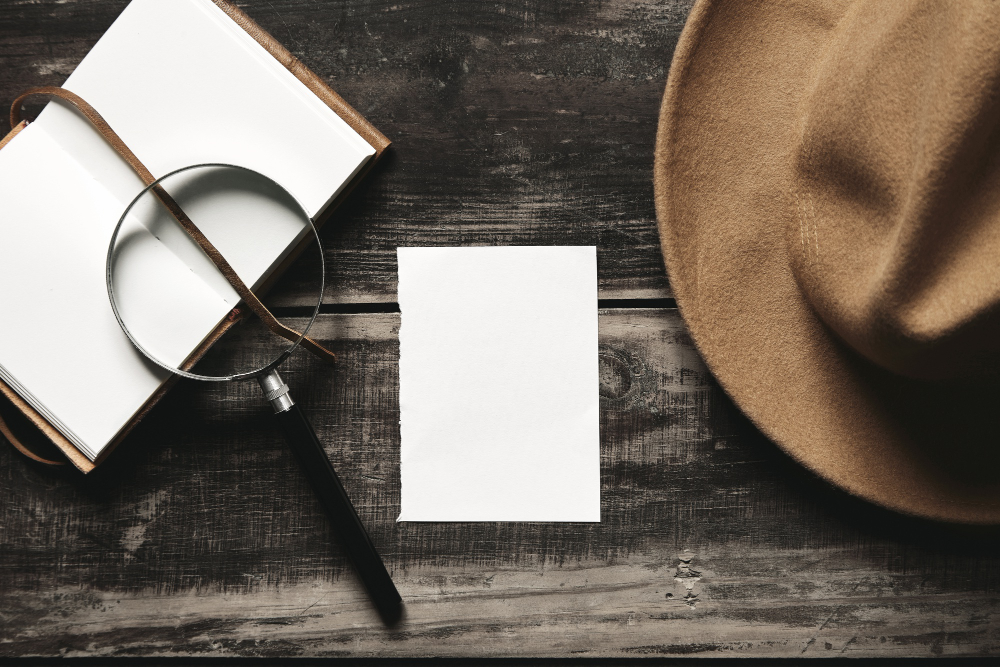 mysterious detective game concept opened notebook leather cover sheet white paper felt brown hat big vintage magnifier steel glasses isolated black aged wood table top view
